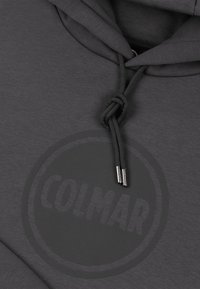 Grå huva med mjuk textur, med en rund logotyp som tydligt visar "COLMAR" i mitten och snören med metalldetaljer.