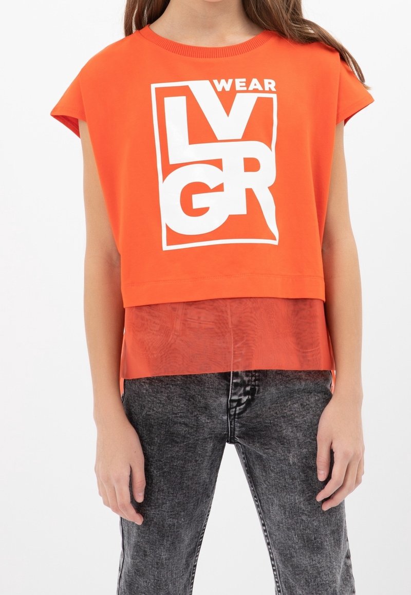 Orange croppet t-shirt med hvid tekst, der har et lagdelt design med en gennemsigtig bund. Kombineret med sorte jeans med en falmet tekstur.