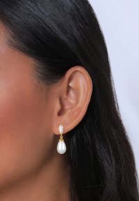 Zlatne naušnice s dijamantom u obliku marquise i bisernim kapljičastim privjeskom, koji ističe glatku teksturu i elegantan dizajn.