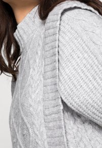 Grå stickad tröja med ett kabelmönster på ena sidan och ribbat tyg på den andra, med hög krage och mjukt, gemytligt material.