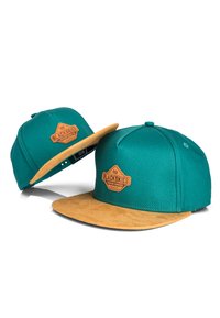Gorra verde azulado con visera de ante color arena, que presenta un parche de cuero marrón con "BLACKSKIES" en relieve. Diseño estructurado, con parte trasera ajustable.