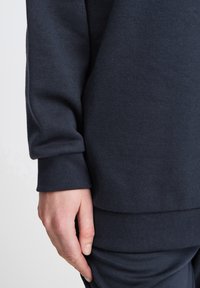Mørkeblå sweatshirt med blød tekstur, ribbede manchetter og lige kant. Nærbillede der viser en hånd på ærmet.