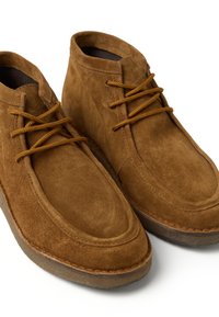Bruine suède enkellaarsjes met bruine veters, ronde neus en een textuur op de bovenkant. Zacht materiaal en een gebogen zool voor comfort.