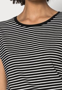 Top a rayas en blanco y negro con cuello redondo y mangas cortas, hecho de una tela suave; las rayas están espaciadas de manera uniforme.