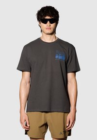 Czarna szara bawełniana koszulka z okrągłym dekoltem, krótkimi rękawami i niebieskim nadrukiem na klatce piersiowej. W połączeniu z beżowymi szortami.