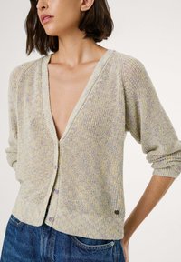 Leicht strukturierte Strickjacke in Pastellfarben, mit einem tiefen V-Ausschnitt, Knopfverschluss und gerippten Bündchen. Auffälliges kleines Logo-Detail am Saum.