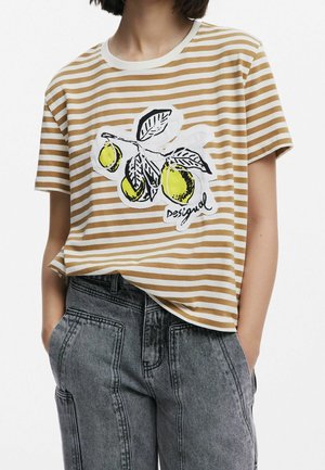 Frau trägt ein beige-weiß gestreiftes T-Shirt mit einem Zitronenzweig-Grafik und dem Schriftzug "Desigual", kombiniert mit grauen, hoch taillierten Jeans.