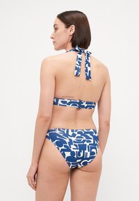 Bikini komplekts ar zilu un baltu abstraktu rakstu. Haltera kakla dizains ar sasaisti un aizmugurējo aizdari. Gluda, elastīga auduma materiāls.