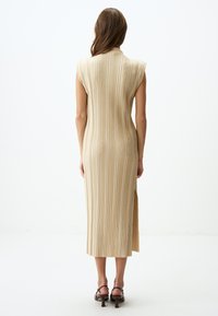 Abito beige a lunghezza ginocchio con texture a coste verticali, colletto alto e maniche a cappuccio. L'apertura laterale e la silhouette aderente ne migliorano il design.