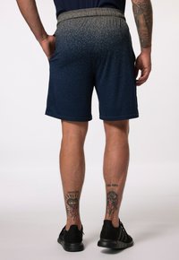 Mandens blå athletic shorts med en spraglet grå talje. Har sidelommer og en glat tekstur. Sorte sneakers på fødderne.