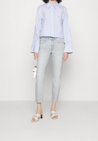 Camisa de botones a rayas azul y blanca con puños anchos, combinada con jeans ajustados de lavado claro y sandalias de tacón bloque en color blanco roto.