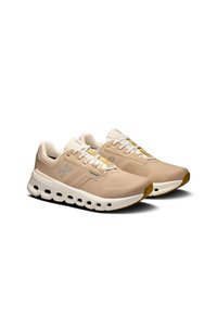 Beige athletic shoes with mesh upper, white sole featuring shock-absorbing pods and gray logo accents. Rounded toe and flat laces.