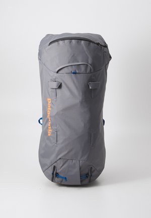 Pelēka mugursoma cilindriskā formā, izgatavota no auduma. Iekļauj augšējo rāvējslēdzēju, zilu akcentu un oranžu logotipu. Satur regulējamas siksnas.