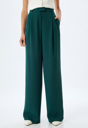 Pantalones de pierna ancha en tela azul profundo. Presentan pliegues, una cintura alta y bolsillos laterales. La textura suave realza el diseño general.
