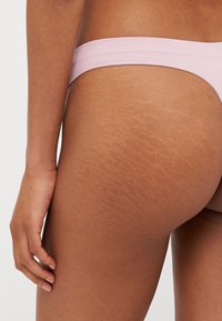 Purple ribbed thong with a soft texture, low-rise design, featuring a smooth waistband and visible skin with stretch marks on the side.