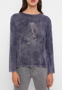 Lila Langarmoberteil mit strukturierter Oberfläche, das in der Mitte ein Strass-Skull-und-Kreuzbones-Design aufweist.