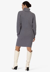 Grijze ribbelgebreide jurk met een hoge kraag, aansluitende silhouet en lange mouwen, gecombineerd met kniehoog witte leren laarzen.