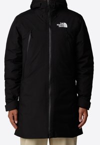 Parka negra impermeable con capucha, que cuenta con dos bolsillos con cremallera, cierre frontal con cremallera y el logo de The North Face en el lado izquierdo del pecho.