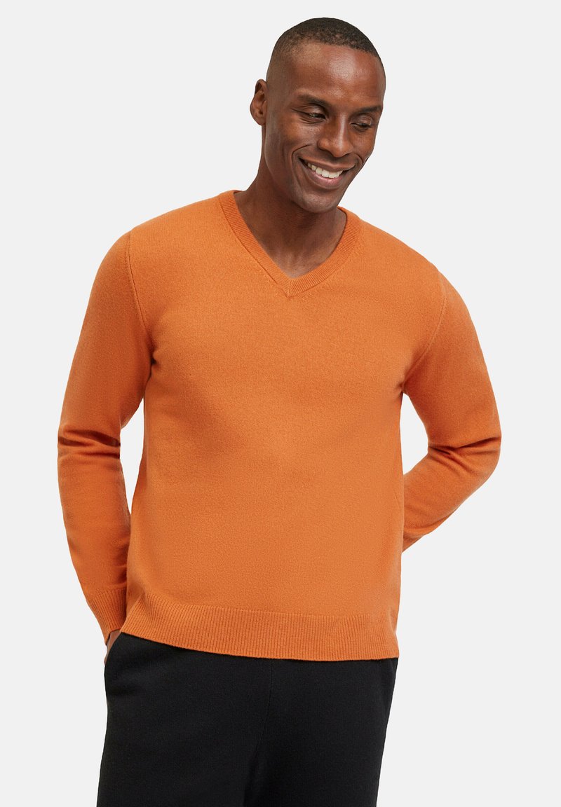 Maglione a V in un brillante colore arancione, realizzato in materiale testurizzato con polsini e orlo a coste, abbinato a pantaloni scuri.