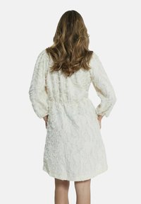 Witte, gestructureerde jurk met een fluffy oppervlak, lange mouwen en een elastische taille. Heeft een knielange snit en een comfortabele pasvorm.