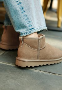 Bottes courtes en daim marron avec une surface texturée, un bout arrondi et une semelle en caoutchouc plate. Les bottes sont dotées d'une petite boucle à l'arrière.