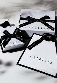 Tre vita presentförpackningar med svart band, som har varumärket "LATELITA" i ett modernt typsnitt, mot en neutral bakgrund.