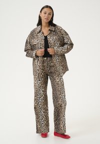 Set di camicia e pantaloni con stampa animale in tonalità beige e nera, caratterizzato da una vestibilità comoda, maniche lunghe e un audace motivo leopardato. Le scarpe rosse completano l'outfit.