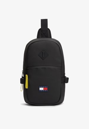 Zaino nero dal design elegante e arrotondato. Presenta un logo Tommy Jeans ben visibile, una tasca frontale con cerniera e una tiretto della cerniera giallo.