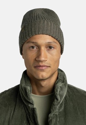 Olivgrüner gestrickter Beanie mit Rippenmuster. Getragen mit einer Cordjacke und einem strukturierten olivgrünen Hemd darunter.
