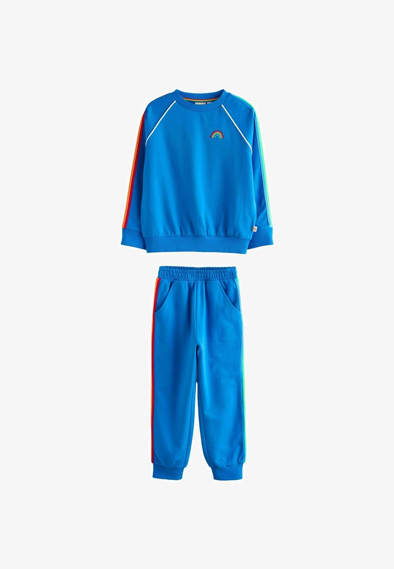 Blå träningsoverall med en crewneck-tröja som har ett litet regnbågsemblem och röd, grön och blå randiga detaljer på ärmarna och byxorna.