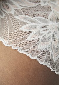 Išskirtinis nėrinių audinys su sudėtingais gėlių raštais balta spalva ir švelniais rožiniais akcentais; banguoti kraštai ir smulkūs, detalūs siuvinėjimai.