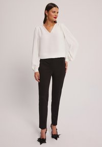 Biała, długa bluzka z długim rękawem i dekoltem w kształcie litery V, zestawiona z dopasowanymi czarnymi spodniami i czarnymi szpilkami z wstążkowymi akcentami.