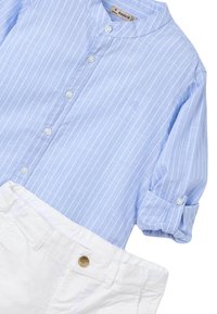 Camisa de color azul claro con cuello y rayas blancas, con cierre de botones y mangas remangadas, combinada con pantalones de algodón blancos con un botón dorado.