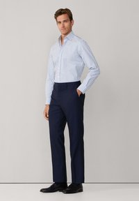 Chemise boutonnée à rayures blanches et bleues avec des manches longues, associée à un pantalon bleu marine. Des chaussures noires complètent la tenue. Texture de tissu lisse.