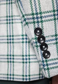 Beżowa marynarka w kratę z zielonymi i niebieskimi wzorami, teksturowany materiał oraz cztery czarne guziki z białym przeszyciem przy mankietach.