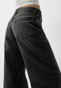 Černé džíny s širokými nohavicemi z denimu s vybledlou texturou, pět kapes a kontrastním prošíváním na pásu a kapsách.