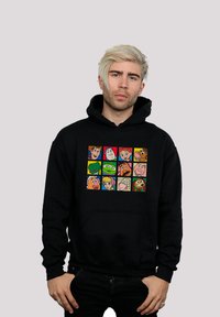 Felpa nera con un grafico frontale che presenta una griglia di volti di personaggi dei cartoni animati in vari colori. Il materiale sembra morbido e strutturato.