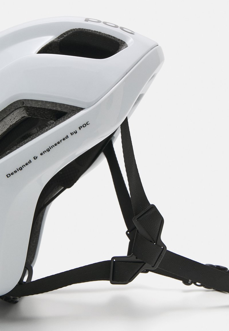 Weißer Helm mit strukturiertem Innenraum, Belüftungsöffnungen, schwarzen Riemen und einer Schnalle. "Entwickelt und konstruiert von POC" auf der Seite gedruckt.