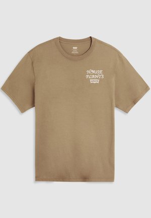 Barna pamut póló rövid ujjakkal és kerek nyakkivágással. Fehér nyomott szöveg található rajta: "HÁZINÖVÉNYEK" egy Levi's címkével alatta.