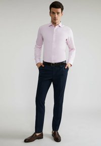 Jasnoróżowa koszula z długim rękawem, ciemnoniebieskie spodnie w kratę, brązowe skórzane buty, elegancki design i dopasowany krój.