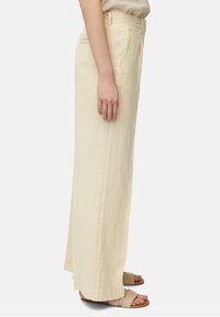 Beige linnen brede-pijpenbroek met een gladde textuur, zijzakken en een getailleerde pasvorm. Gecombineerd met lichtbruine platte sandalen.