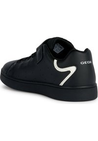 Sneaker in pelle nera con una superficie liscia, caratterizzato da un accento curvo bianco, perforazioni sui lati e una chiusura a strappo.