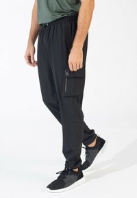 Zwarte joggerbroeken met een elastische tailleband, een ritszak aan de zijkant en een slim fit. Gemaakt van lichtgewicht stof met een zachte textuur.