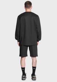 Czarna koszulka z długim rękawem i dopasowane szorty wykonane z gładkiego materiału, zestawione z czarnymi skarpetkami i trampkami z zielonymi akcentami. Prosty design.