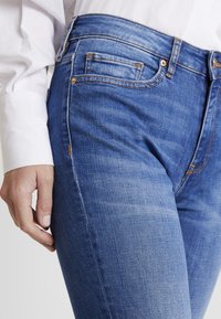 Blå denimjeans med slim fit, som har detaljer i gyllene färg, fyra fickor och synliga sömdetaljer. Mjuk textur och en något bleknad finish.