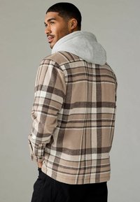 Ruttet flannelskjorte i beige, brun og krem med en grå hætte. Struktureret stof, knaplukning ved ærmerne og en afslappet pasform.