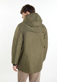 Giacca impermeabile verde oliva con cappuccio, texture liscia e polsini regolabili. Presenta una ventilazione posteriore e un orlo dritto.