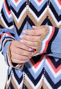 Stickad tröja med ett chevronmönster i nyanser av blått, brunt, marinblått, röd och vitt. Har detaljer med öppet stickning och texturerade ärmar.