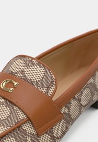 Brown patterned loafers with a leather strap and a gold logo detail. The upper features a textured fabric design with a smooth lining.