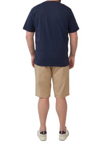Marineblauwe katoenen T-shirt met korte mouwen, gecombineerd met beige shorts. Het model draagt lichtgekleurde sneakers met een contrasterende accent.